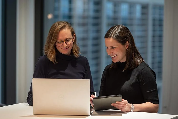 Two people looking at a tablet beside an open laptop