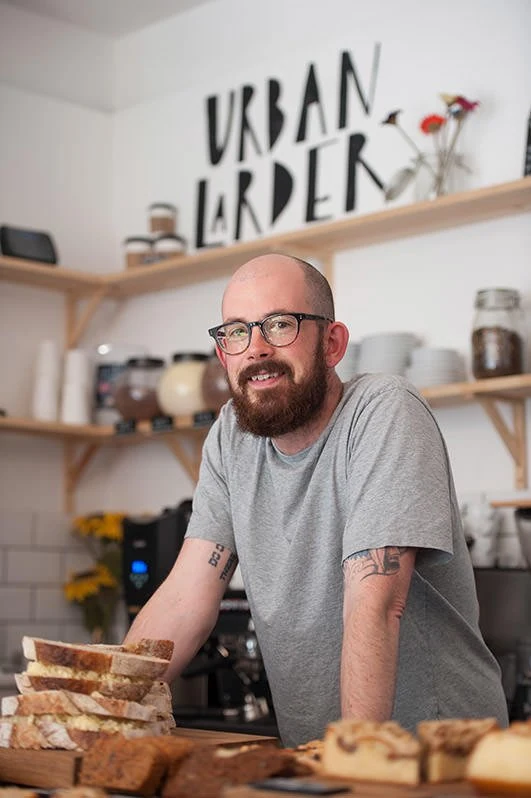 Man behind a food counter with Urban Larder signage in the background