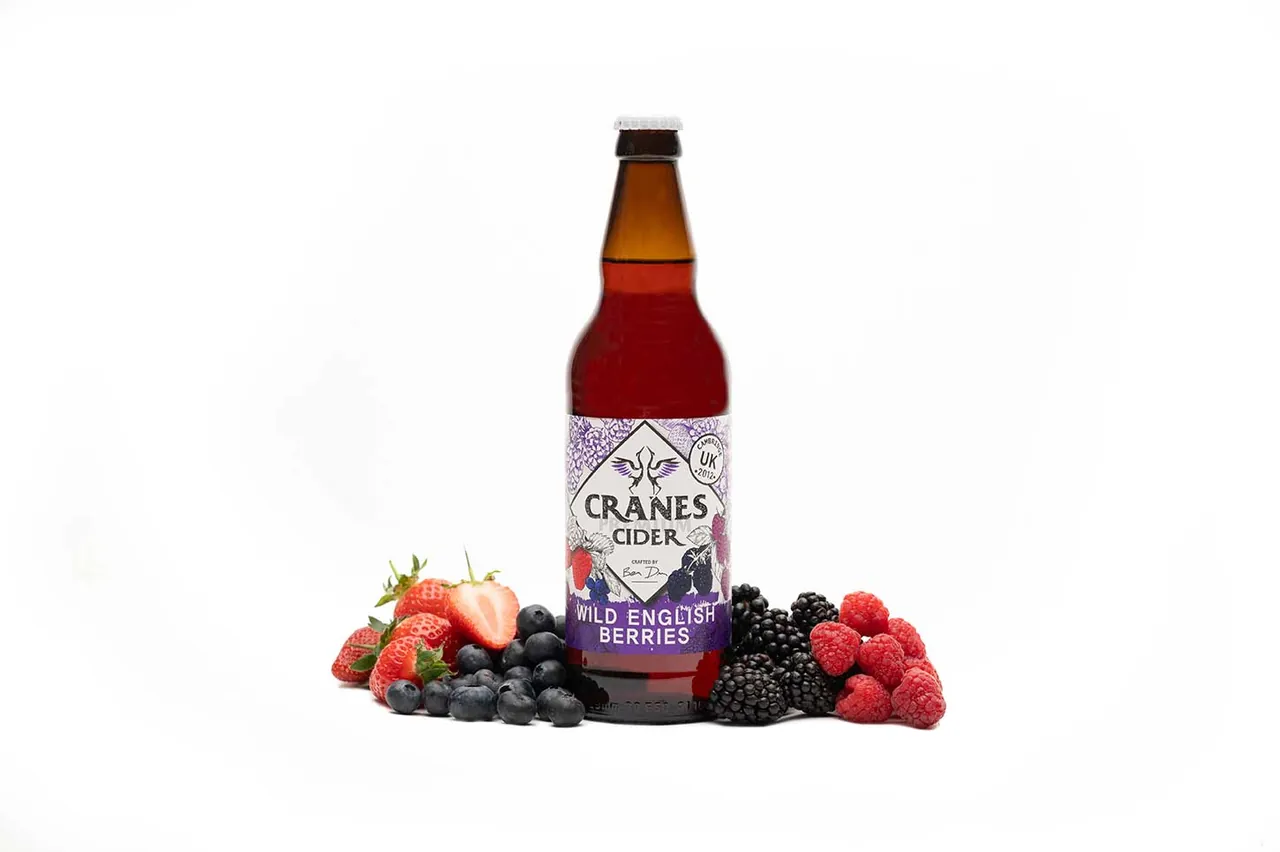 A bottle of Cranes wild English berries cider surrounded by fresh berries on a white background