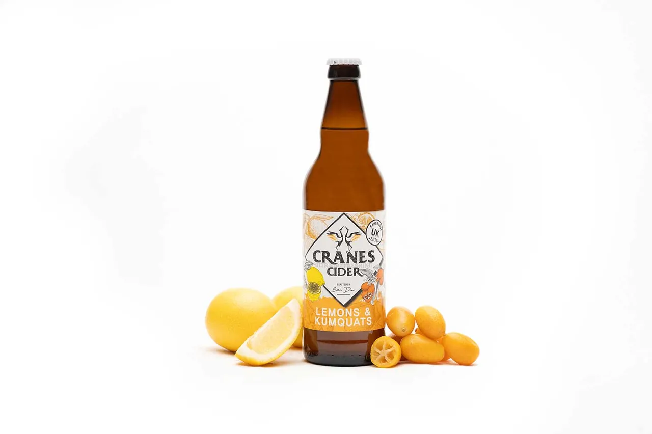 A bottle of Cranes lemon and kumquat cider with fresh citrus fruit on a white background