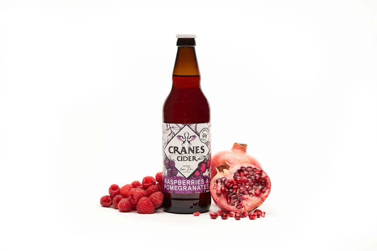 A bottle of Cranes raspberry and pomegranate cider with fruit on a white background