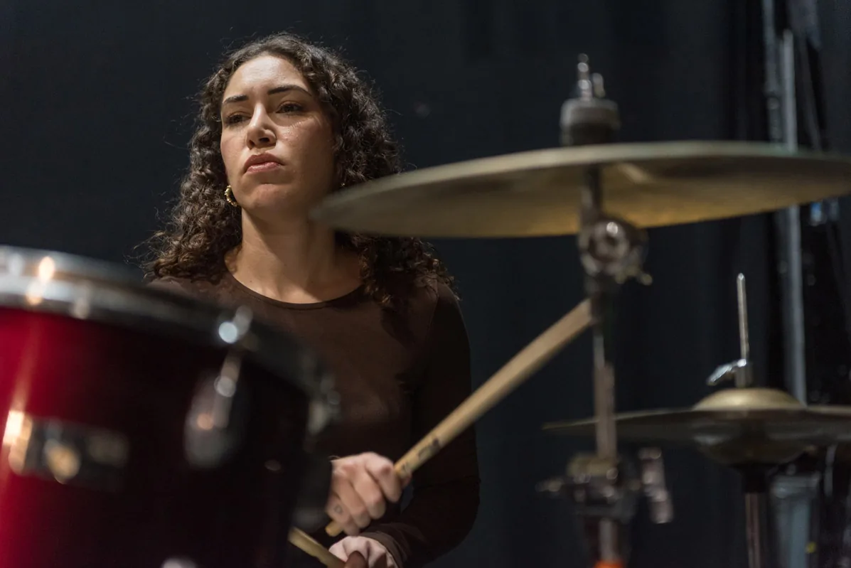 A drummer playing on a dark stage, lit from the side