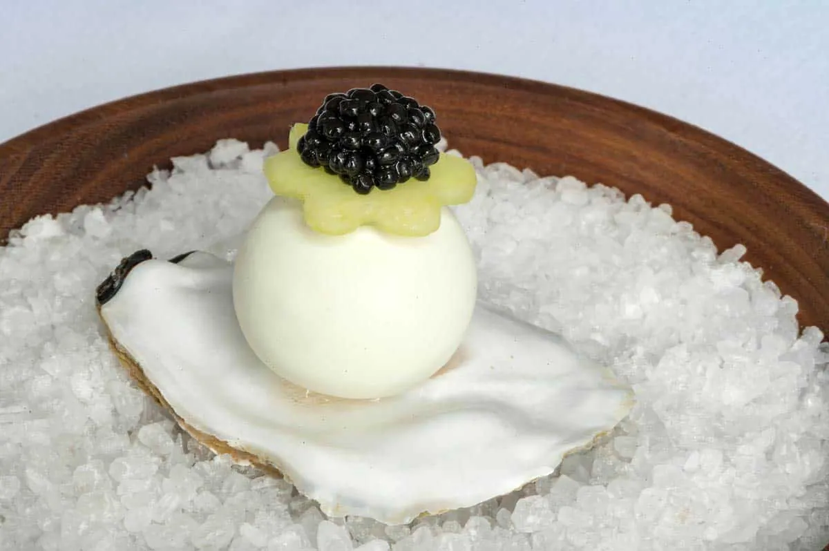 An oyster shell on rock salt topped with a white sphere and caviar