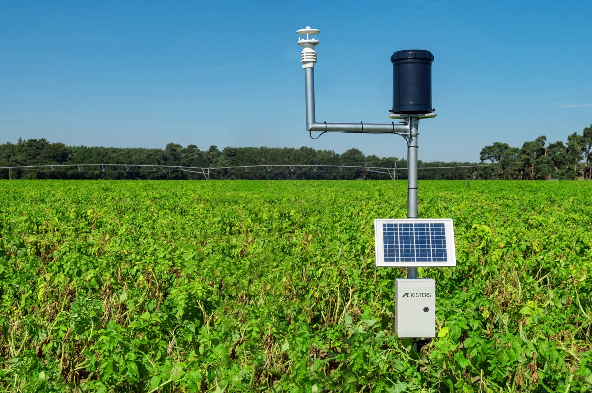 A Kisters environmental monitoring station with a solar panel standing in a green field under a blue sky