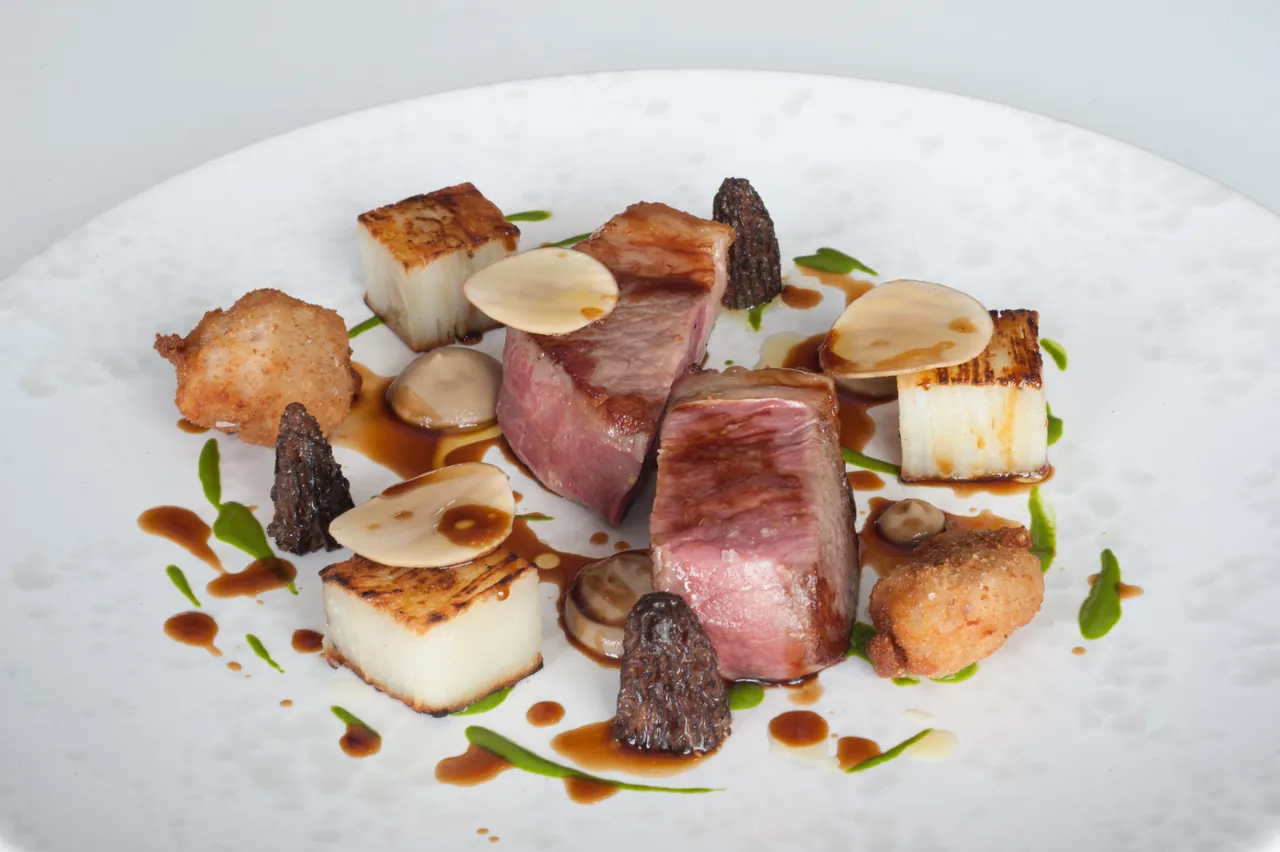 A plated dish of lamb with vegetables and sauce on a white plate