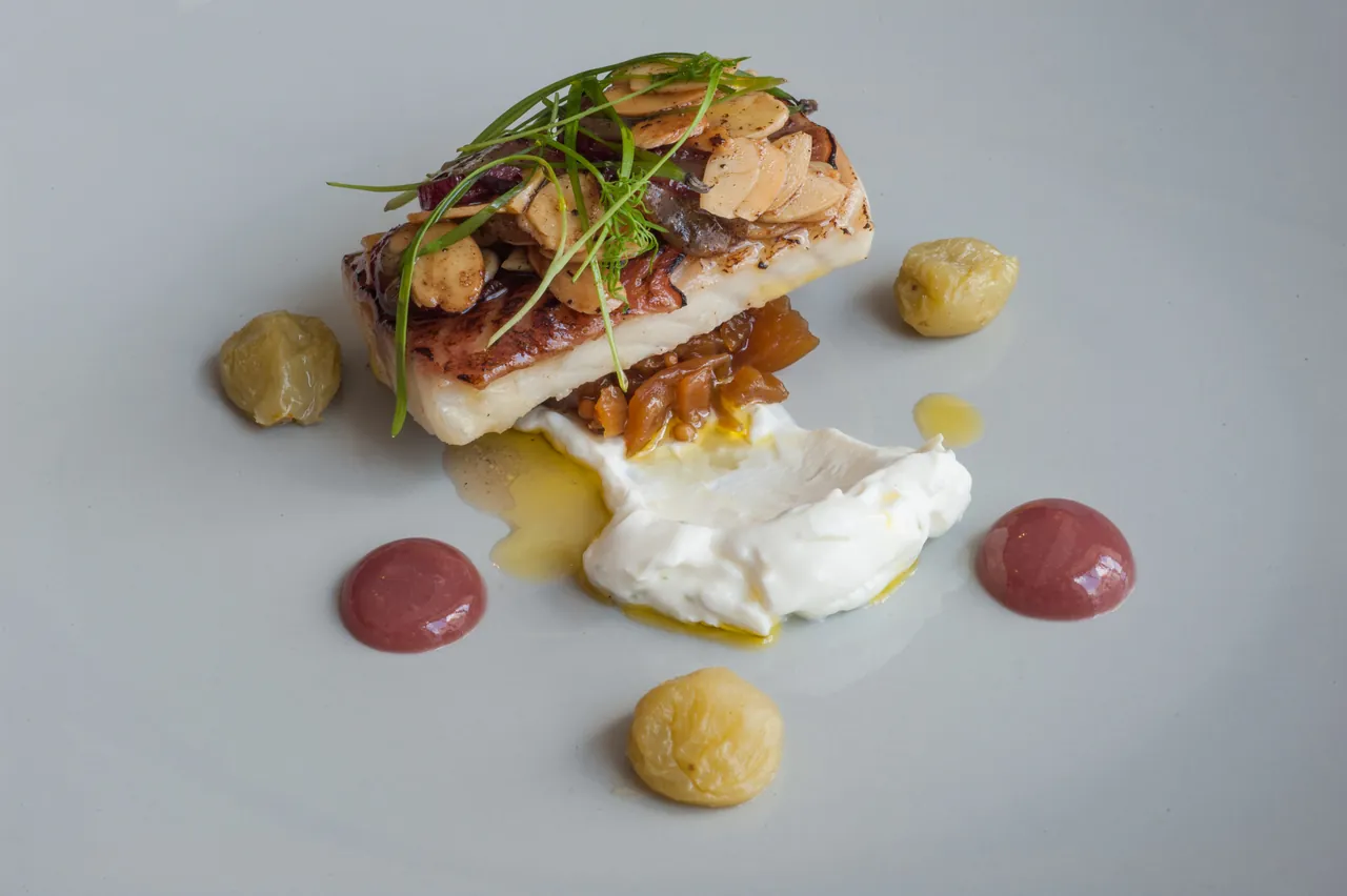 A fish dish with small garnishes on a white plate