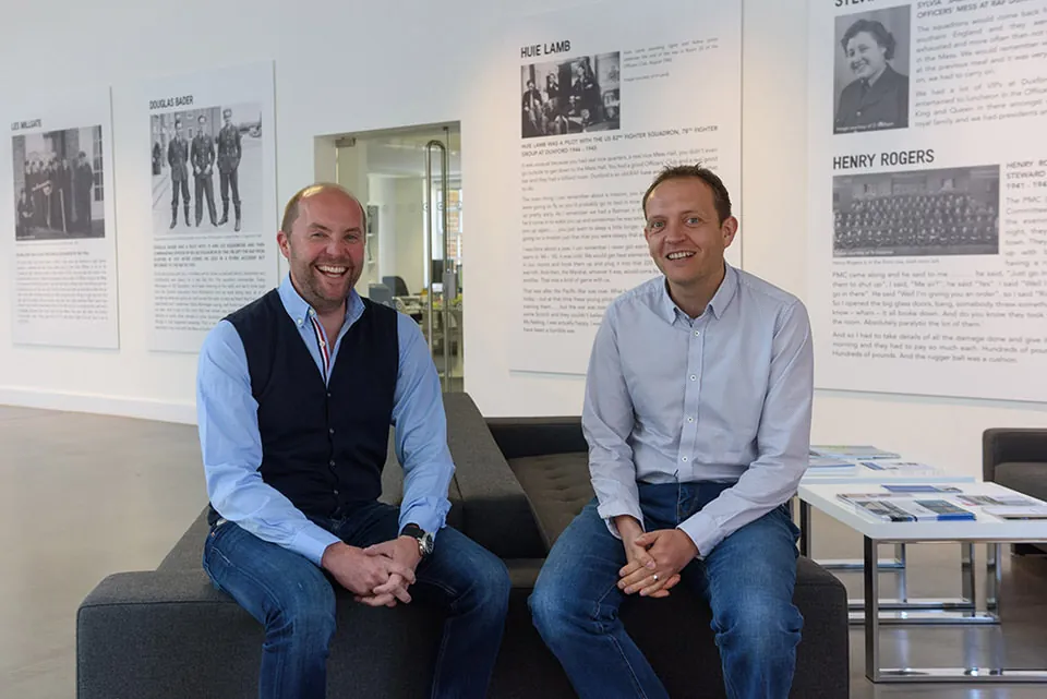 Two business leaders seated in conversation in front of a display wall