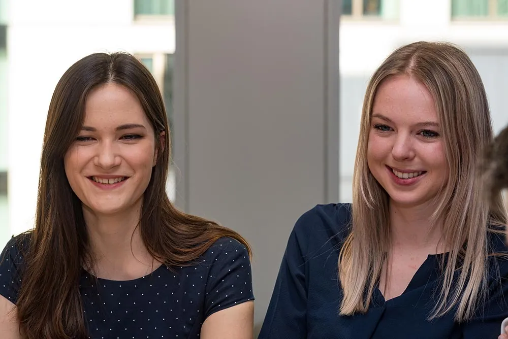 Two young colleagues smiling side by side in an office