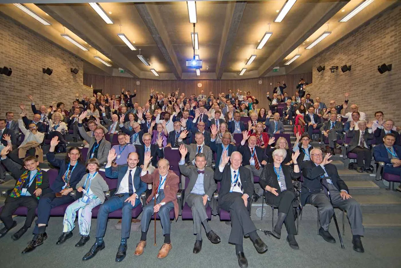 A conference audience waving for the group photograph in a tiered lecture theatre