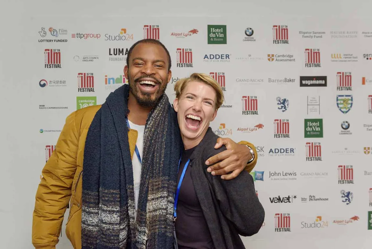 Two guests laughing together in front of the Cambridge Film Festival sponsor wall