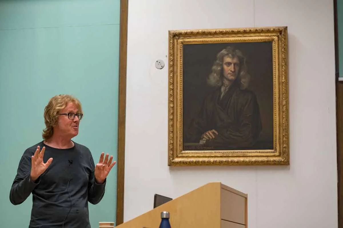 A speaker presenting beside a portrait of Isaac Newton at a mathematical conference