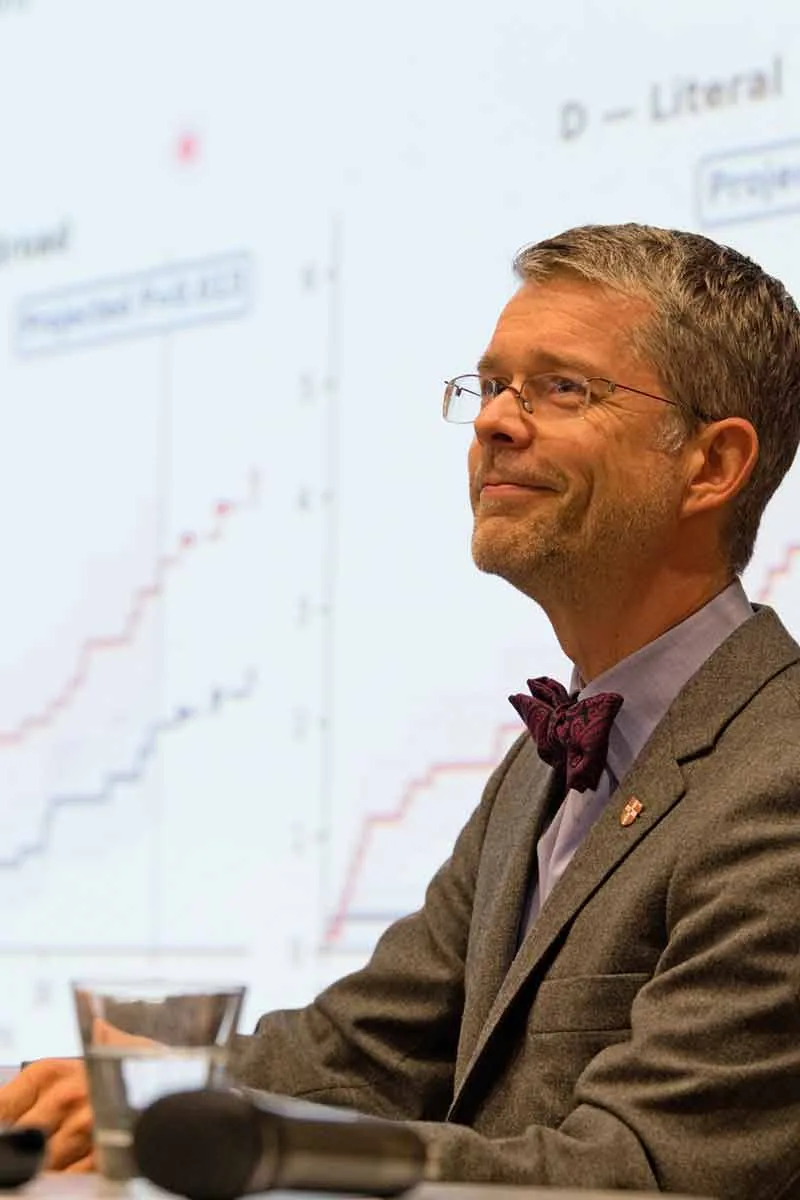 A panellist in a bow tie smiling in front of a projected chart
