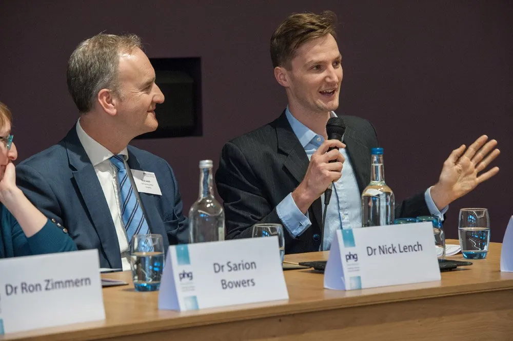 Two panellists speaking at a conference table with name cards and microphones