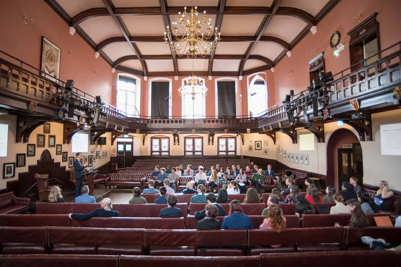 A talk in the Cambridge Union debating chamber, with the audience on leather benches beneath the chandeliers