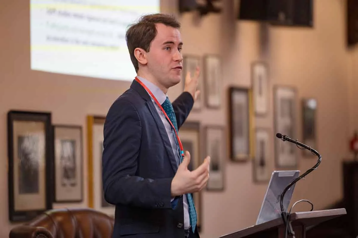 A speaker at the lectern in the Cambridge Union, gesturing towards his slides