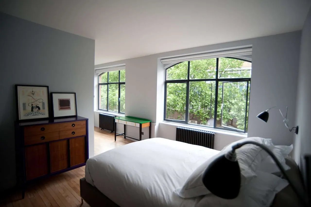A bright bedroom with large steel-framed windows onto a garden