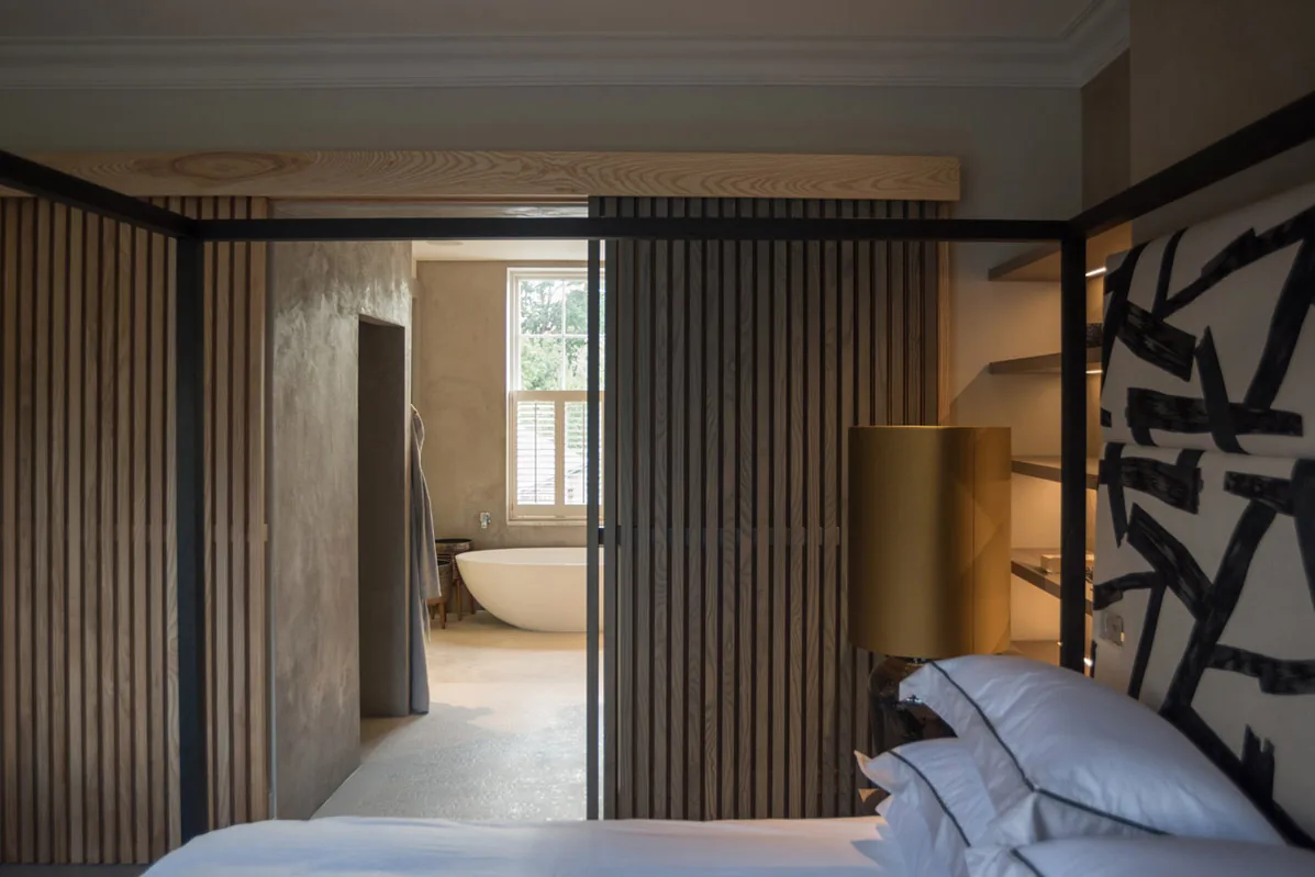 A calm bedroom with a timber-slatted partition and an open bathroom beyond