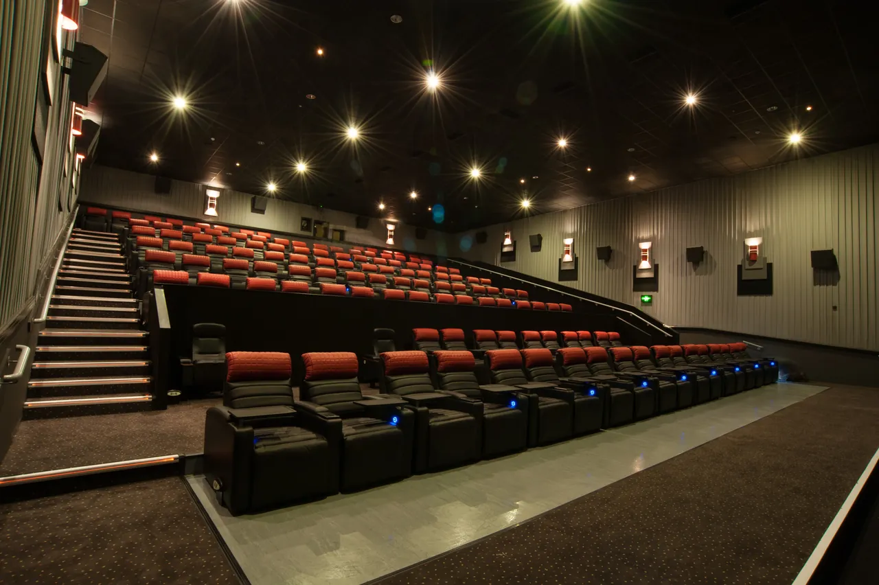 A cinema auditorium with rows of red reclining seats and ceiling lights