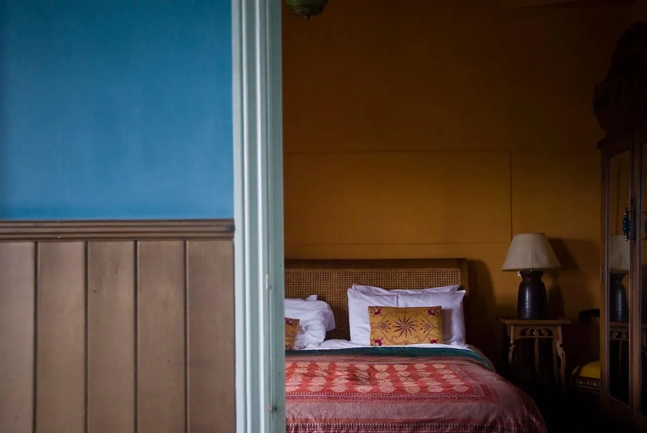 A hotel bedroom with blue walls, timber panelling and lamps
