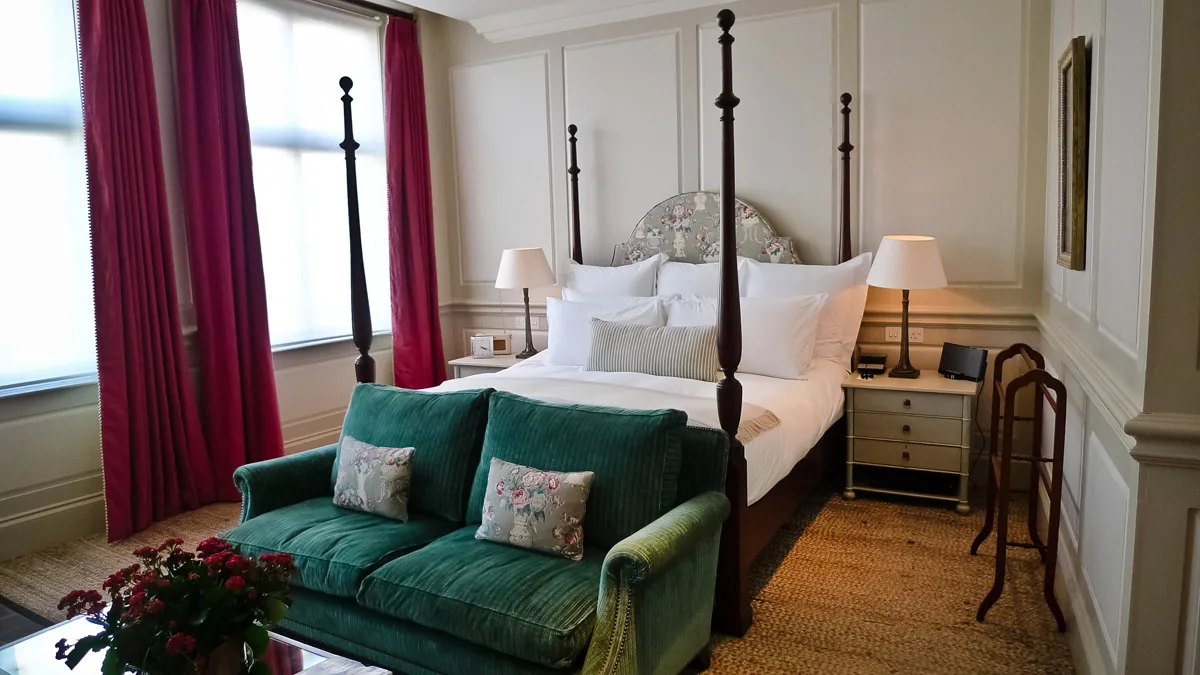 A hotel bedroom with a four-poster bed, green sofa and red curtains