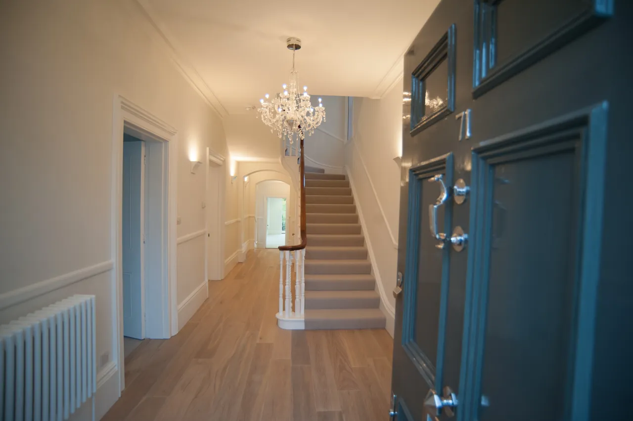 A bright hallway with a chandelier, staircase and dark blue door