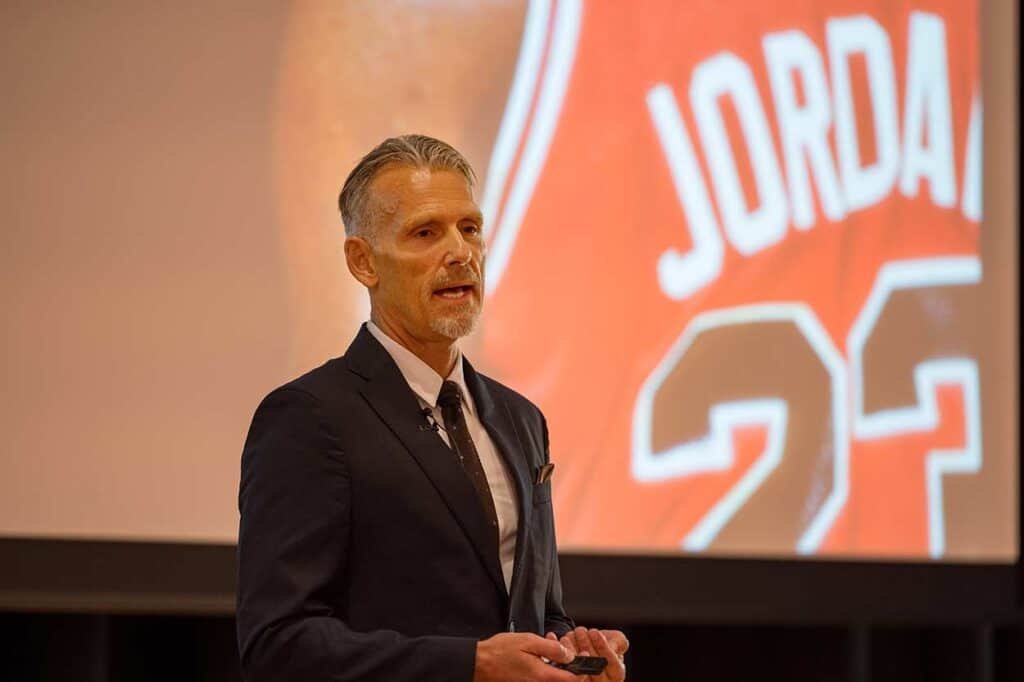 Business professional giving a presentation at corporate event in front of branding screen SEO keywords corporate photographers, business event photography, professional portraits, corporate meetings, UK corporate photography.