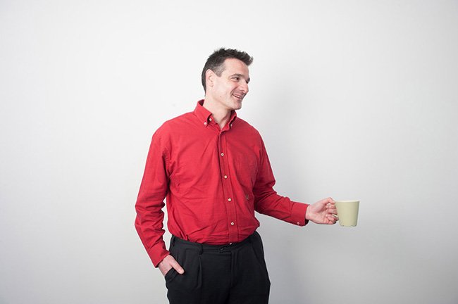 Professional corporate headshot of a man in a red shirt holding a coffee mug.