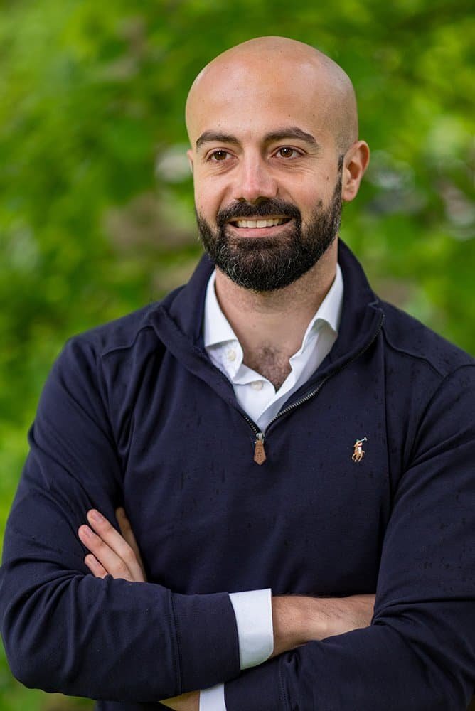 Portrait of a smiling businessman with crossed arms in a natural outdoor setting.