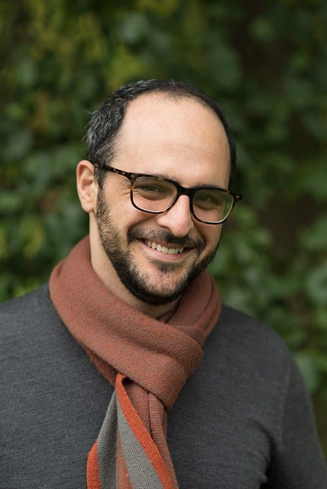 Portrait of a smiling man wearing glasses and a scarf outdoors.
